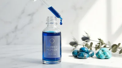 A dropper releasing a drop of bright blue GHK-Cu copper peptide serum above an open bottle on white marble