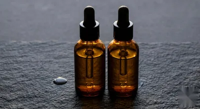 Two amber glass serum dropper bottles side by side on dark slate