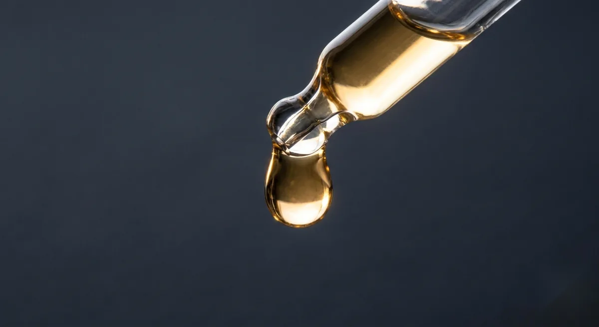 A golden vitamin C serum drop falling from a glass dropper against a dark background
